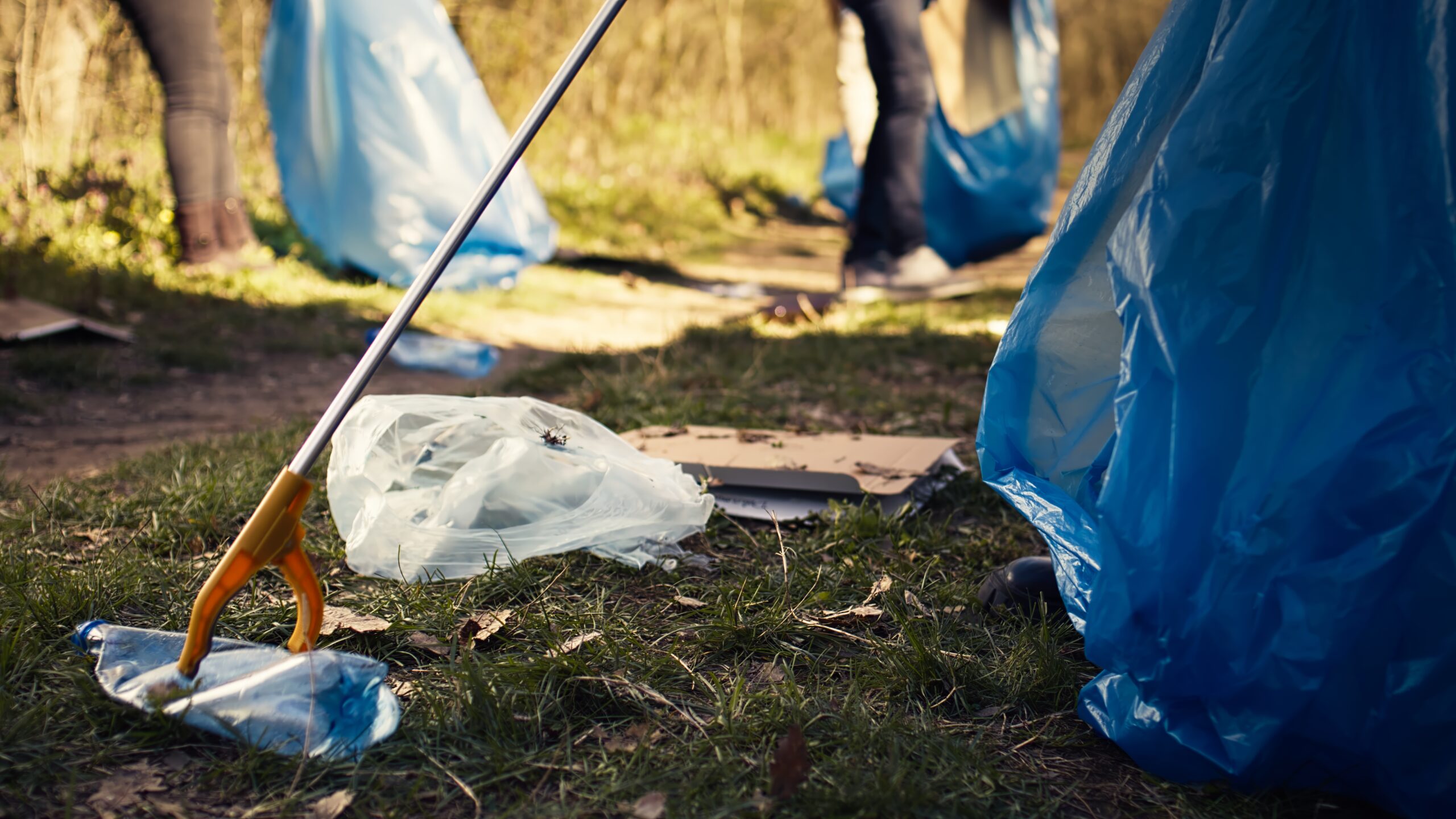 volunteer-using-tongs-tool-collect-trash-plastic-waste-from-woods-scaled